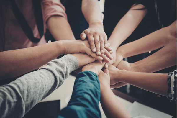 A group of people with their hands stacked on top of each other in a sign of unity and teamwork.