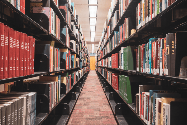 A wide aisle in a library with tall bookshelves filled with books on both sides, receding into the distance.